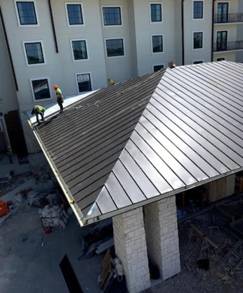 Crew installing standing seam metal roof panels on a commercial project in Willis